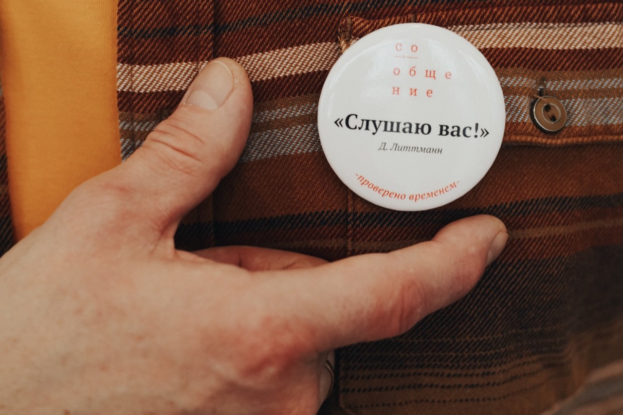 Значок школы «СоОбщение» с надписью «Слушаю вас!» на кармане клетчатой рубашки